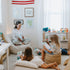 Woman reading to two children in a cozy room with toys and books.